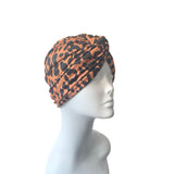 Patterned orange and black twist turban hat for women.